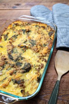 a casserole dish with spinach and sausage in it next to a wooden spoon