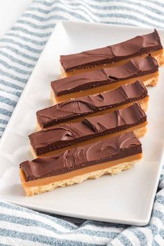 three pieces of chocolate peanut butter bars on a white plate with blue and white striped towel