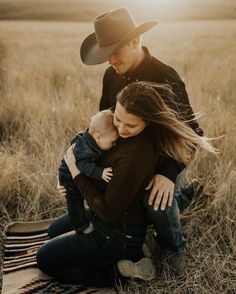 a man and woman holding a baby while sitting on a blanket in the middle of a field