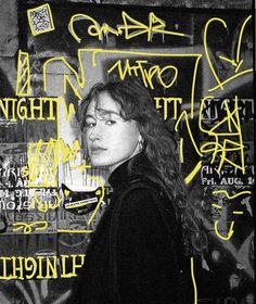 a woman standing in front of a wall covered in graffitti and yellow letters