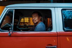 a man sitting in the passenger seat of a red van with his hand on the steering wheel