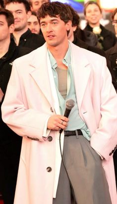 a man standing in front of a crowd holding a microphone and wearing a white coat