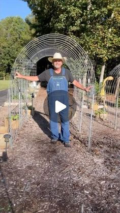 a man in overalls and hat standing next to an open wire fence with his arms outstretched