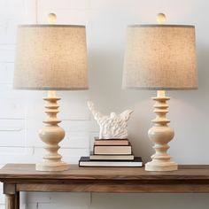 two lamps sitting on top of a wooden table next to a book and lamp shade