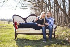 a man and woman sitting on top of a couch in the middle of a field