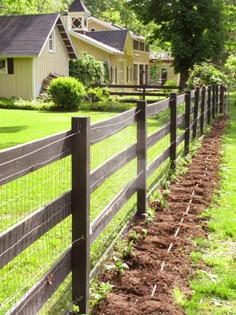 a wooden fence with grass and dirt in front of a house on the other side