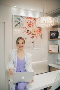 a woman sitting at a table with a laptop computer in front of her and a chandelier hanging from the ceiling