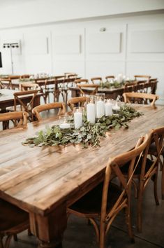 a wooden table with candles and greenery on it in front of a white wall