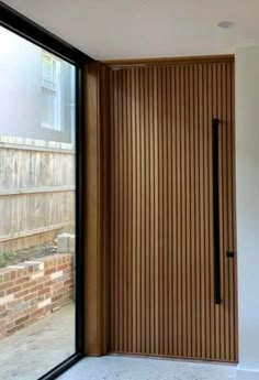 a wooden door is open in front of a brick wall and glass window that looks out onto the backyard