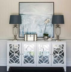 a white sideboard with two lamps and a painting on the wall