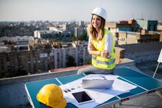 a woman in yellow vest and hard hat sitting at a table with construction equipment on it