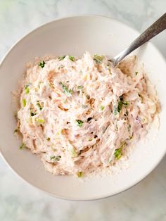 a white bowl filled with tuna salad on top of a marble counter next to a silver spoon