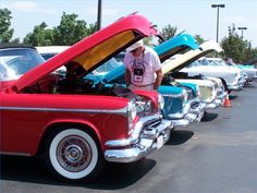 a man standing next to a red car with its hood open and other cars in the background