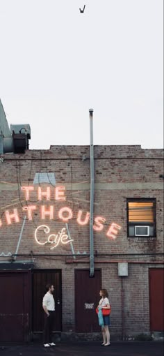 two people standing in front of a building with the words the lighthouse cafe painted on it