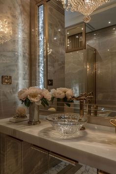 a bathroom with a sink, chandelier and flowers in the bowl on the counter