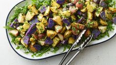 a white plate topped with purple potatoes and green lettuce next to a fork