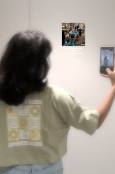 a woman is looking at an image on the wall with her cell phone in hand