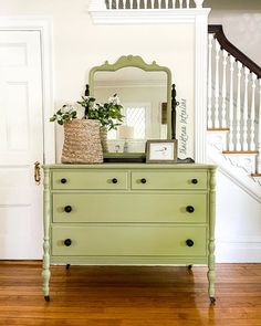 a green dresser sitting in front of a white staircase with a mirror on top of it