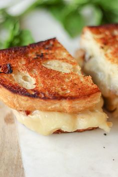 two grilled cheese sandwiches sitting on top of a cutting board next to green leaves