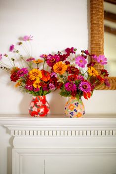 two vases filled with colorful flowers on top of a mantle