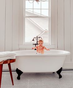 a baby sitting in a white bathtub next to a window