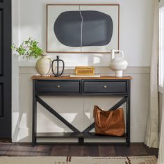 a black and white console table with two vases, a brown bag and a painting on the wall