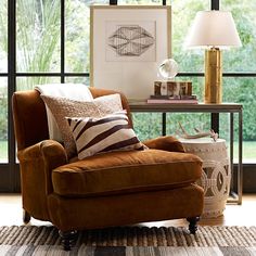 a brown chair sitting in front of a window next to a table with a lamp on it