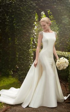 a woman in a white wedding dress standing on a path with flowers and greenery behind her