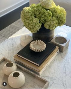 a table topped with books and vases filled with green hydrangeas on top of each other