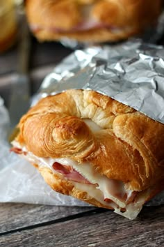 a ham and cheese croissant wrapped in aluminum foil on a wooden table with other pastries