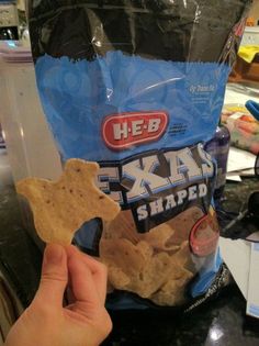 a hand holding a bag of crackers in front of a counter top with other snacks on it