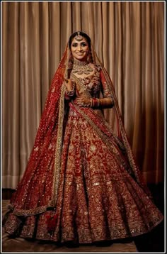 a woman in a red and gold bridal gown posing for the camera with her hands on her hips