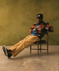 a man sitting in a chair with his legs crossed, wearing a baseball cap and khaki pants