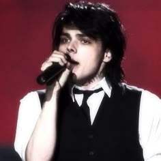 a man with black hair is holding a microphone in his hand and wearing a vest