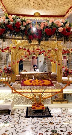 a man sitting in front of a golden altar surrounded by red and white flowers on the floor