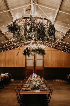 an indoor wedding reception with lights and greenery hanging from the ceiling, surrounded by wood paneling