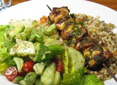 a white plate topped with salad and chicken on top of rice next to a fork