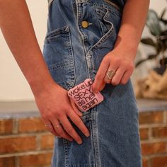 a person holding a pink object with writing on it's side, in front of a brick wall