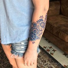 a person with a flower tattoo on their arm and leg, standing in front of a couch