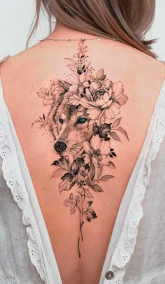 a woman's back with flowers and a wolf tattoo