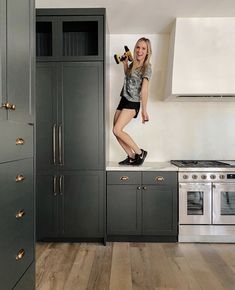 a woman standing on top of a kitchen counter next to an oven and stovetop