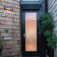 a black door is in front of a brown house with plants on the side walk