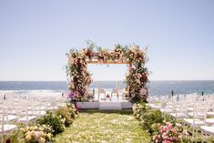 an outdoor ceremony set up with white chairs and pink flowers on the aisle, overlooking the ocean