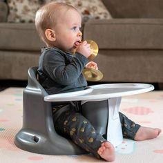 a baby sitting in a high chair eating food from a toy spoon while looking at the camera