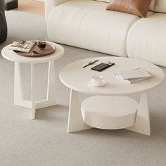 two tables sitting on top of a carpeted living room floor next to a white couch