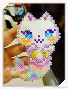 a person holding up a small piece of art made from perler beads that looks like a cat