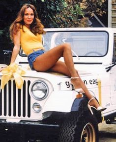 a woman sitting on the hood of a white jeep with a bow around her waist