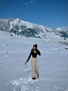 a woman standing in the snow with skis on her feet and mountains in the background