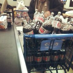 a man standing next to a shopping cart filled with bottled water and soda bottles in a grocery store