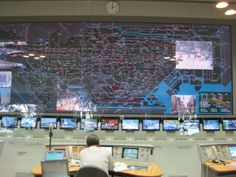 a man sitting at a desk in front of a large screen with multiple monitors on it